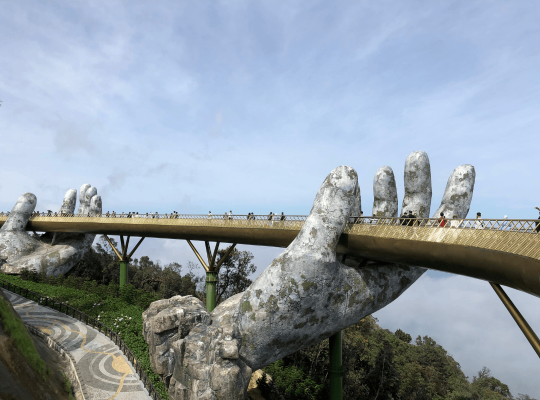 The famous Golden Bridge in Da Nang, Vietnam, held up by giant stone hands, with visitors walking along its golden pathway high above the mountains.